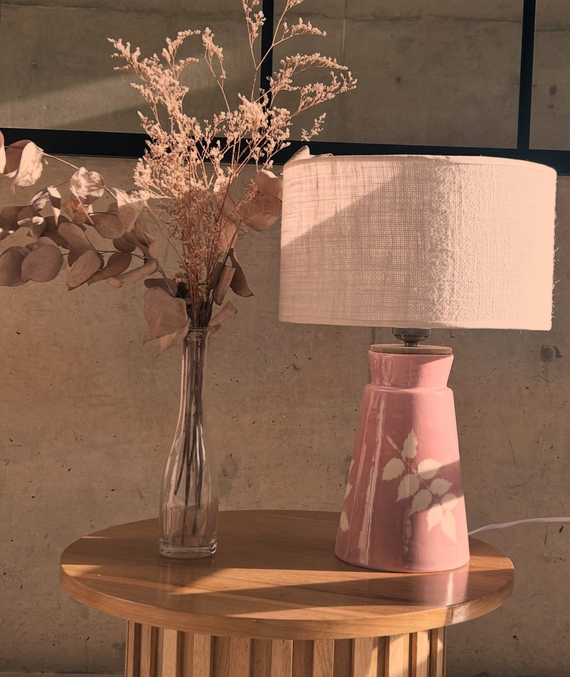 Lámpara de cerámica esmaltada en rosa con motivo de hojas, sobre una mesa de madera junto a un ramo de flores secas