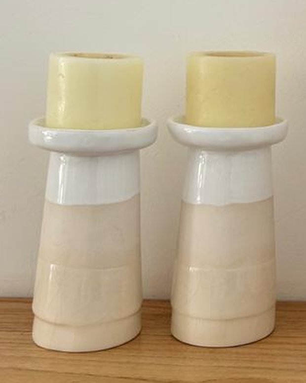 Par de candeleros de cerámica en dos tonos, blanco arriba y arena abajo, con velas gruesas